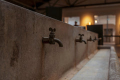 Jimmy Liao - Close-up of rustic taps on a stone sink inside an old workshop, evoking a retro industrial feel.