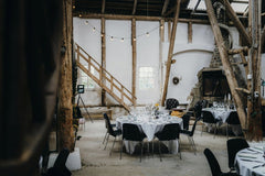 Rene Terp - Charming rustic wedding reception setup in a barn with round tables and minimalistic decor.