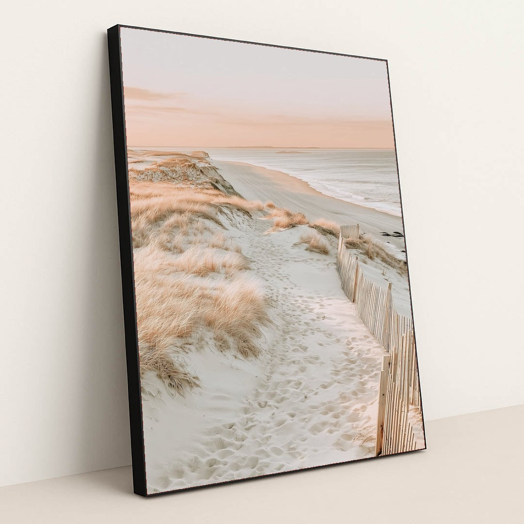 This artwork features a sandy beach path through coastal grass with soft pink light, in a black frame.