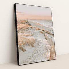 This artwork features a sandy beach path through coastal grass with soft pink light, in a black frame.
