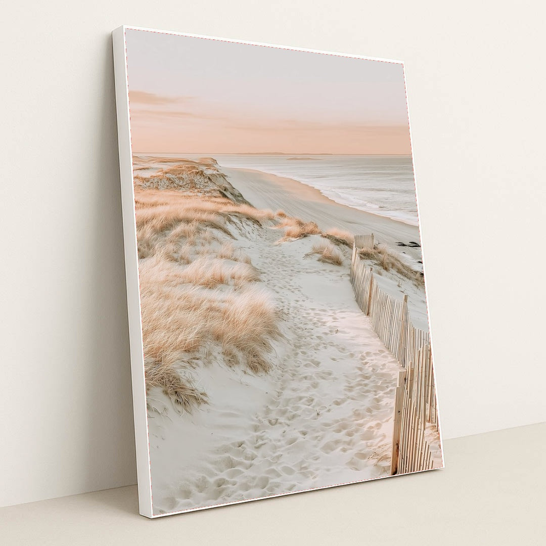 This artwork features a sandy beach path through coastal grass with soft pink light, in a white frame.