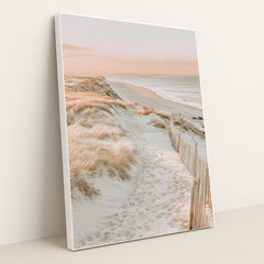 This artwork features a sandy beach path through coastal grass with soft pink light, in a white frame.