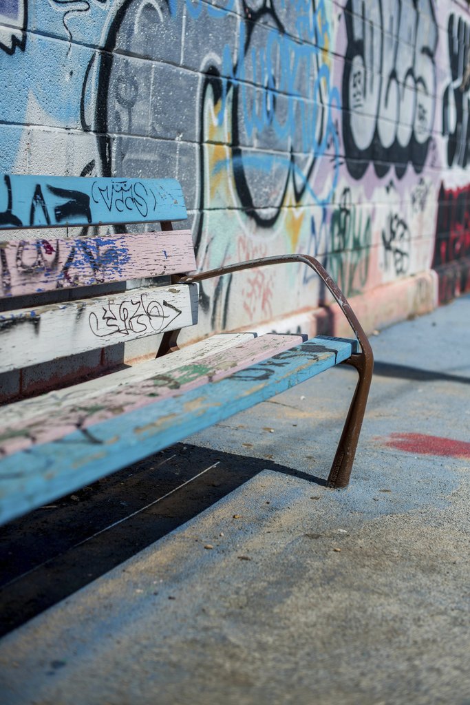 Victor  Moragriega - A colorful graffiti-covered wall with a weathered bench in an urban setting. Artistic street vibe.