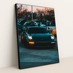 This photo shows a black Porsche 911 with LED headlights at dusk, parked at a car meet with people and vehicles in the background, in a black frame.