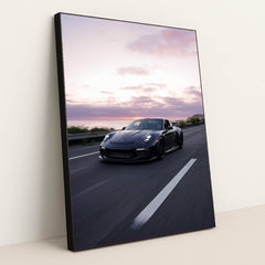 This photo shows a silver Porsche sports car driving on a winding mountain road at sunset, in a black frame.