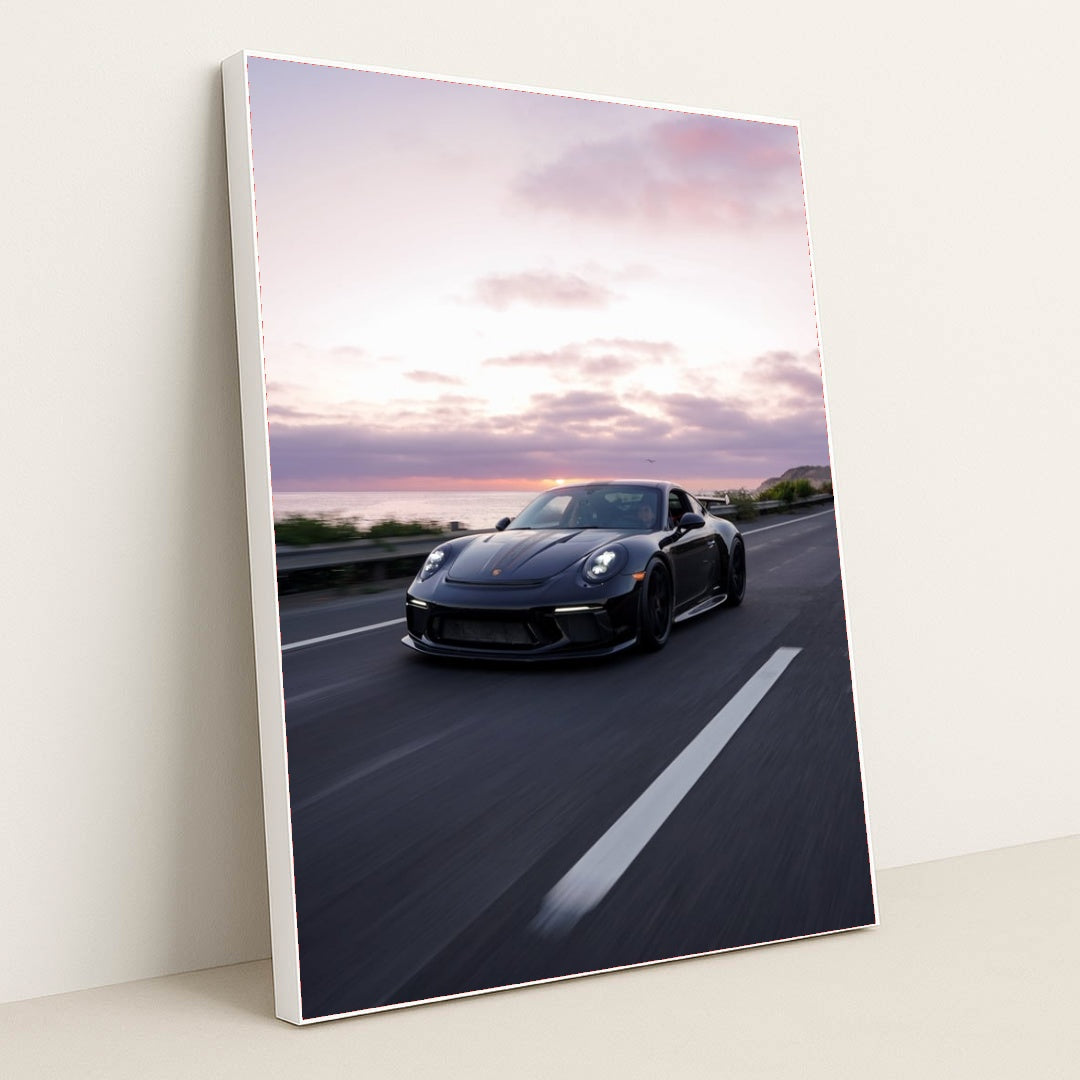 This photo shows a silver Porsche sports car driving on a winding mountain road at sunset, in a white frame.