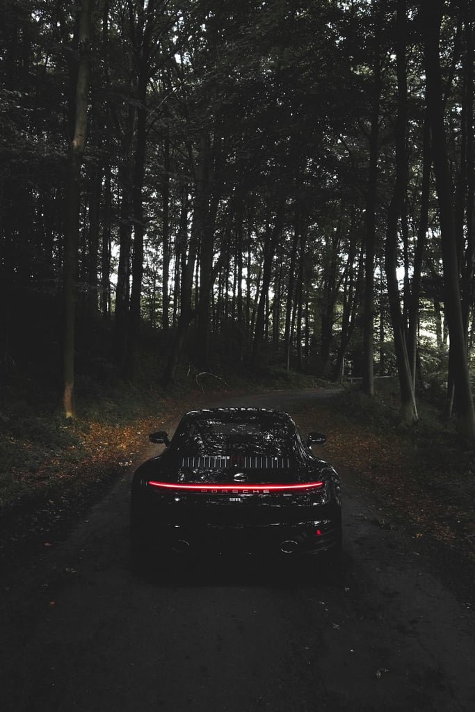 Porsche 911 Taillight Glow in the Woods - rear view of a sleek black car in a dark forest with glowing LED taillights.