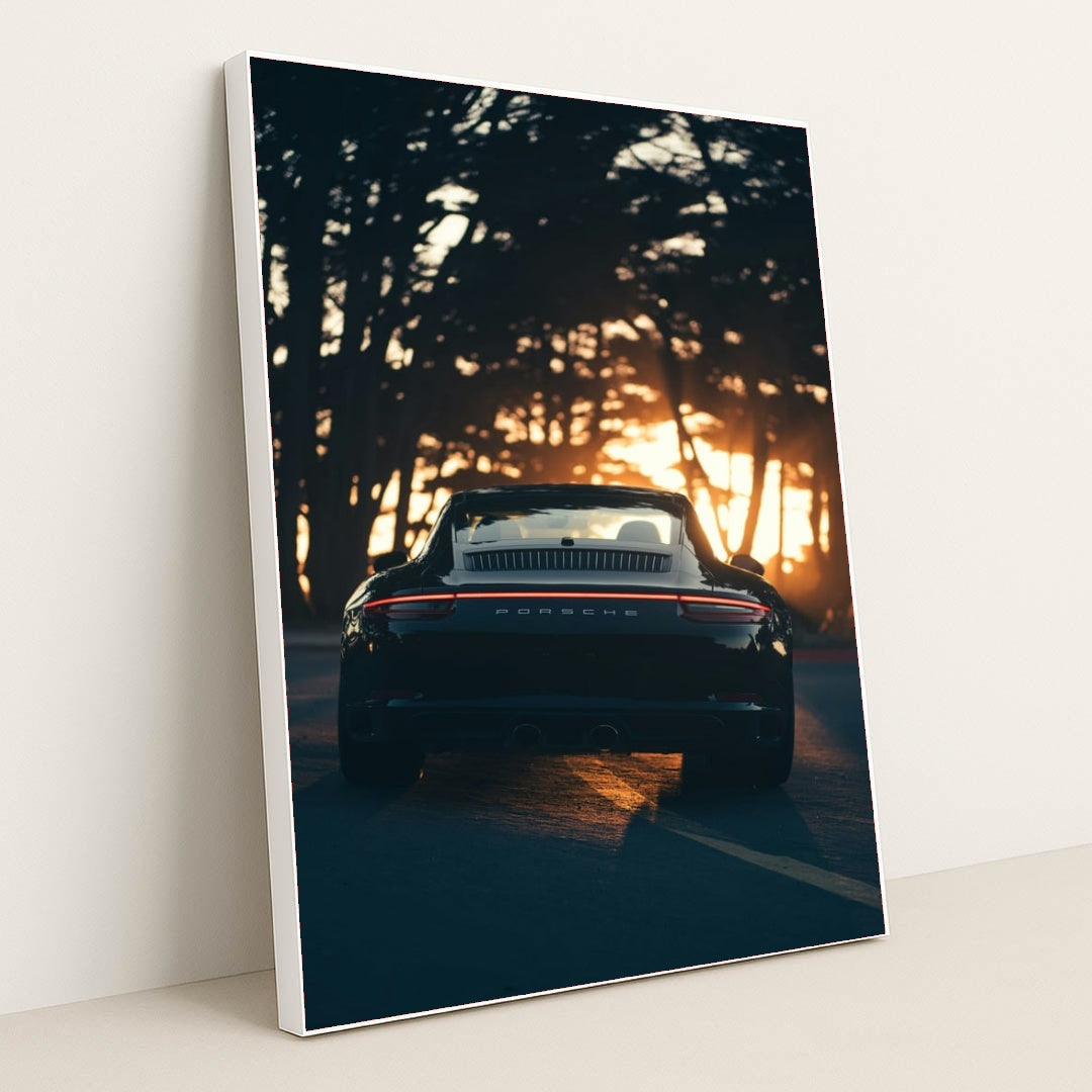 This photo shows the rear view of a black convertible Porsche parked on a tree-lined road at sunset, in a white frame.