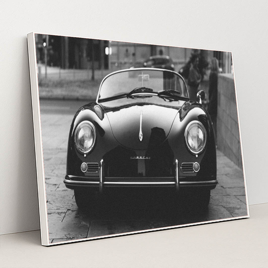 This photo shows a classic black Porsche Speedster convertible parked on a city street in black and white, in a white frame.