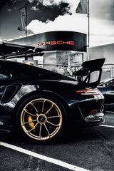 GT2 Outside Porsche parked in front of dealership, showcasing its sleek design and gold wheels, ideal for car wall art.