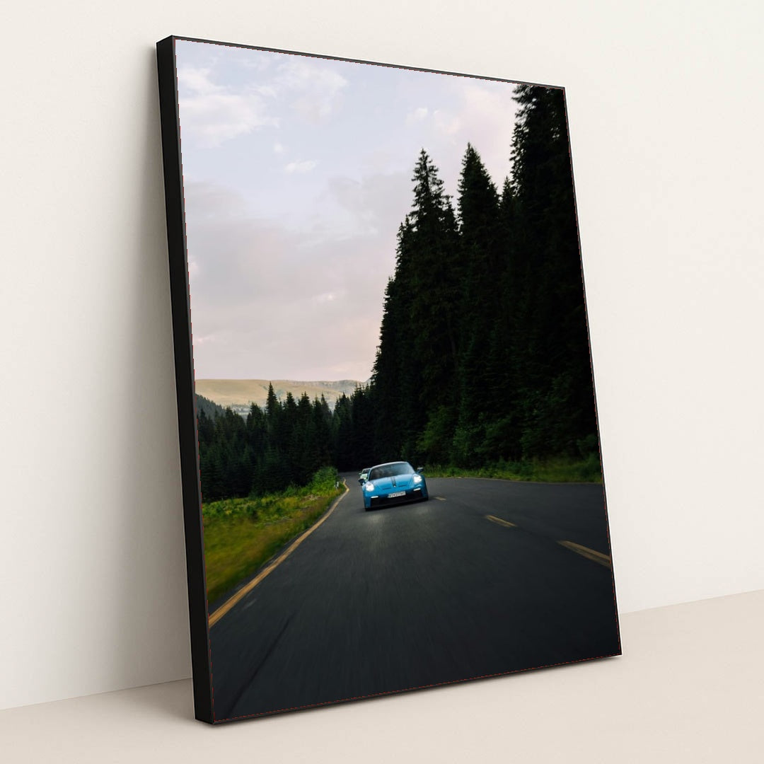 This photo shows a blue Porsche sports car driving on a curvy forest road at dusk, in a black frame.