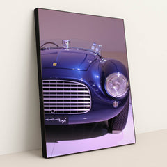 This photo shows the front left side of a blue vintage Ferrari convertible under display lights, in a black frame.
