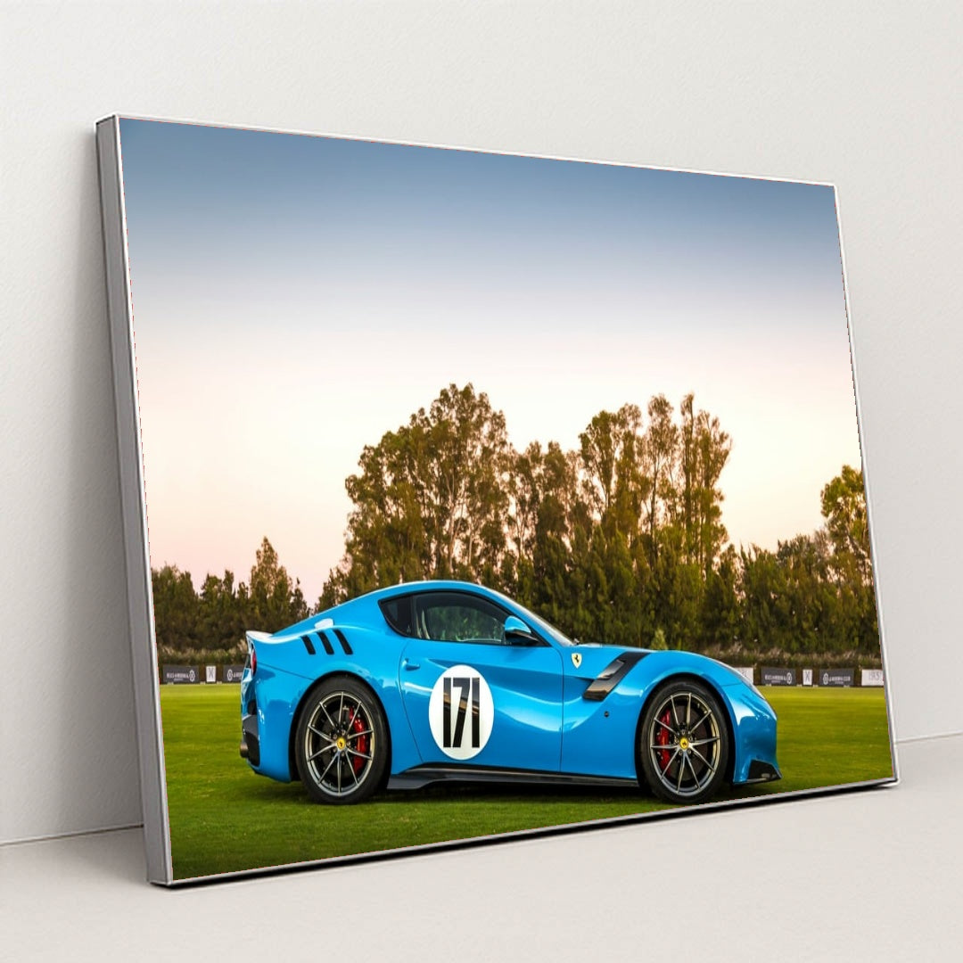 This photo shows a blue Ferrari sports car with racing stripes and the number 171 parked on grass at sunset, in a silver frame.