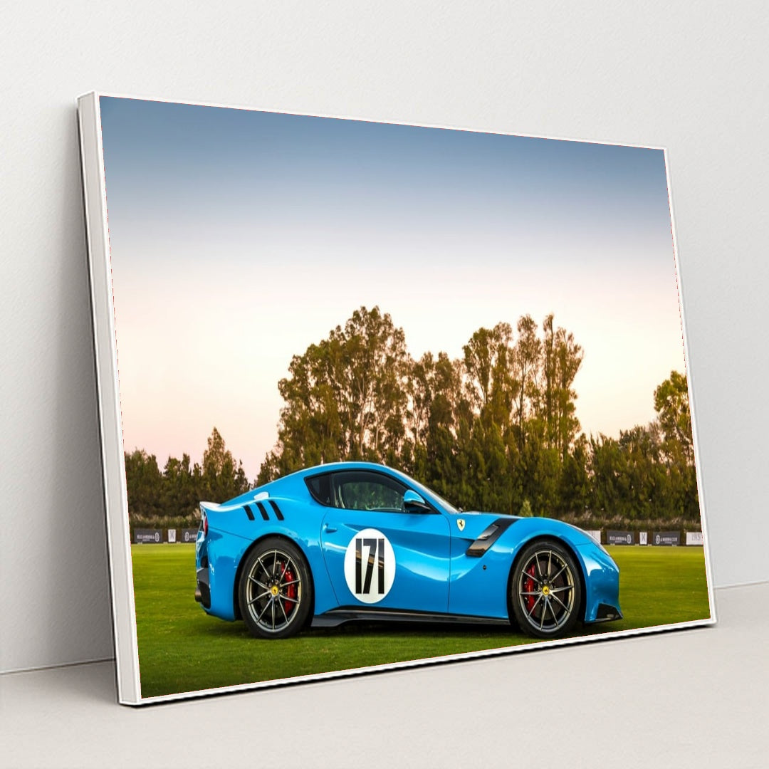 This photo shows a blue Ferrari sports car with racing stripes and the number 171 parked on grass at sunset, in a white frame.