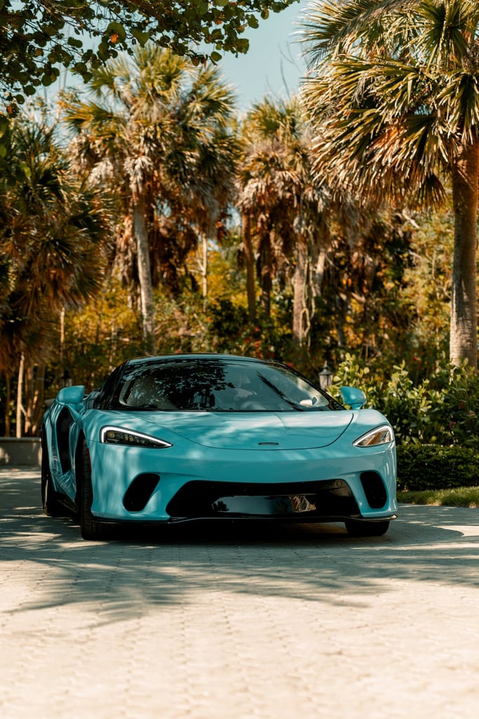 A striking blue McLaren sports car parked among lush palm trees, showcasing luxury in a tropical setting.