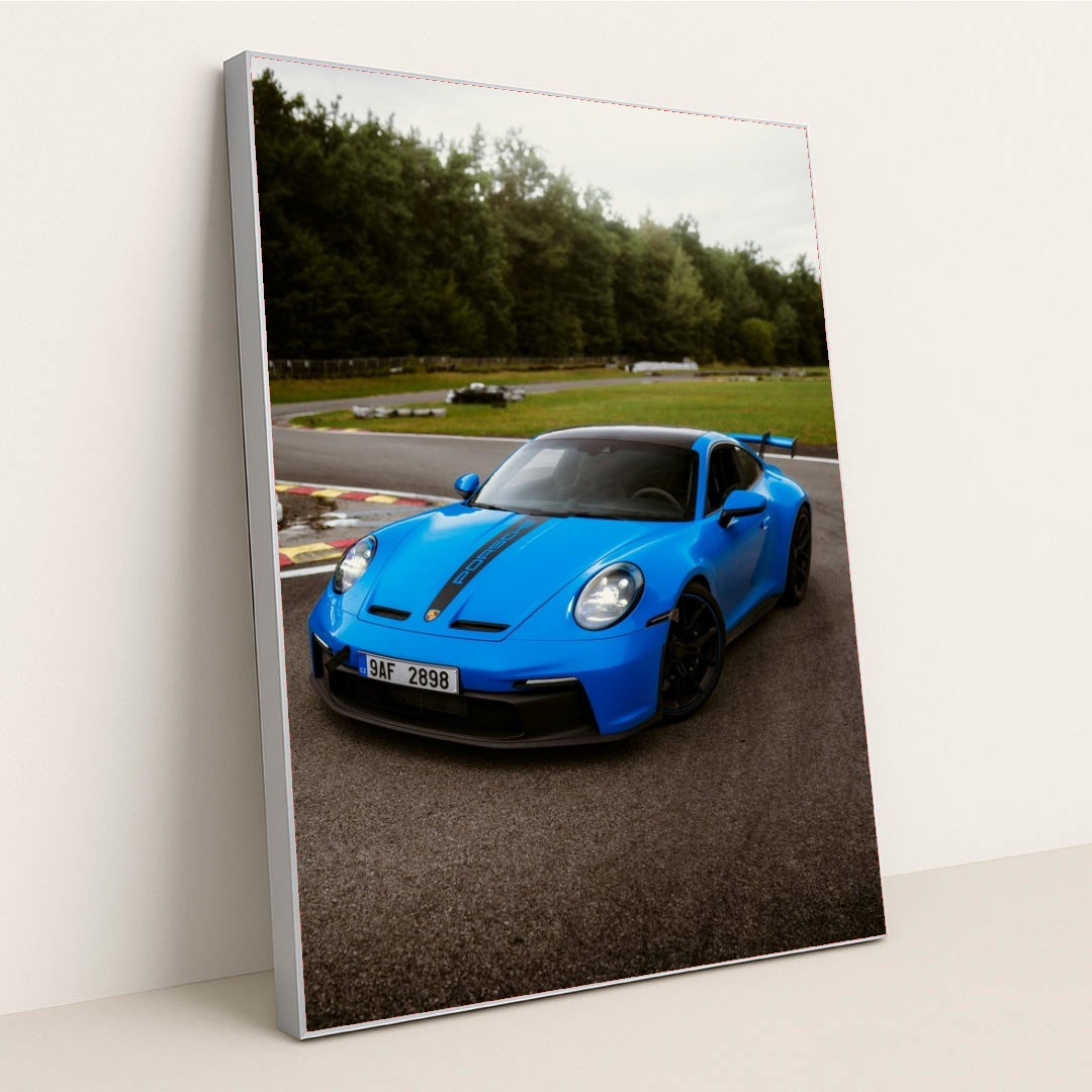 This photo shows a bright blue Porsche 911 GT3 with black racing stripes parked on a curvy racetrack, in a silver frame.