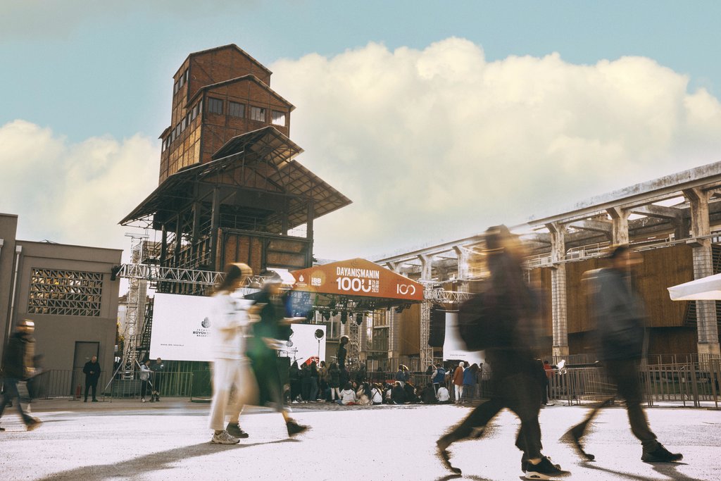 Sami TÜRK - Blurred crowd walking by a historic gasworks and tower in Istanbul, Turkey.