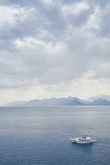 Engin Akyurt - A lone boat sails across a tranquil sea beneath cloudy skies and distant mountains.