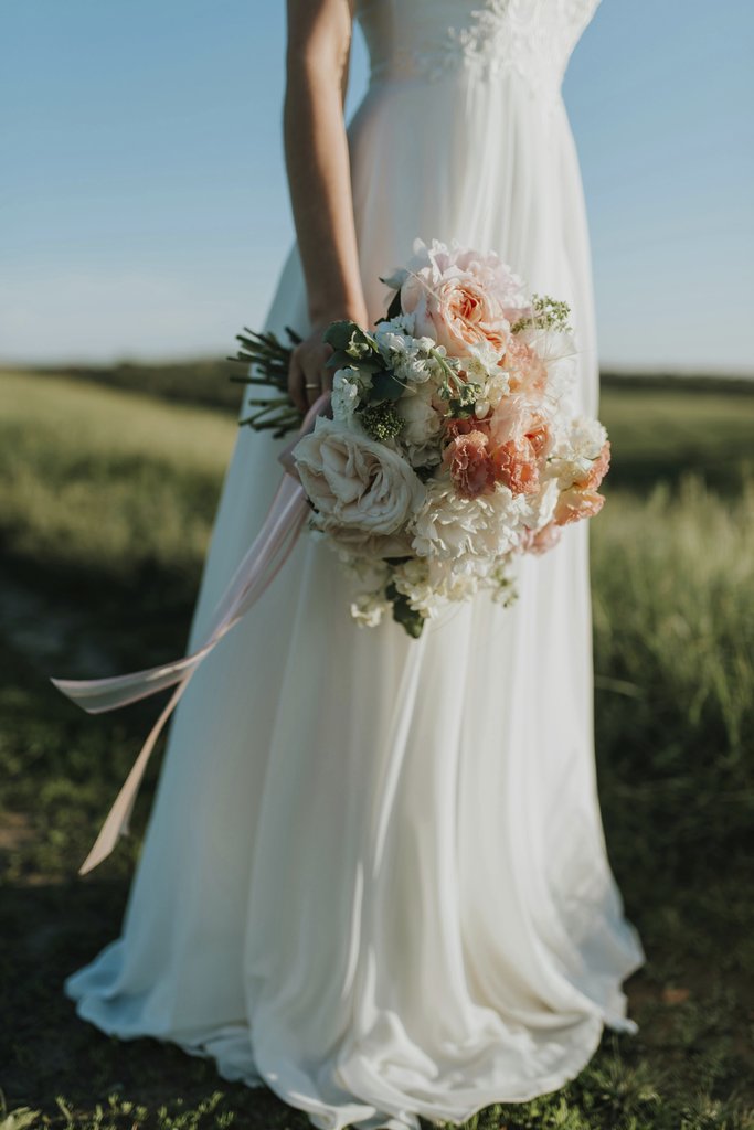 Dmitry Zvolskiy - A bride in a flowing white gown holds a colorful bouquet in a sunny field.