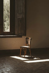 Fernando  Cortes - A rustic wooden chair bathed in sunlight by an old wooden window, creating a serene atmosphere.