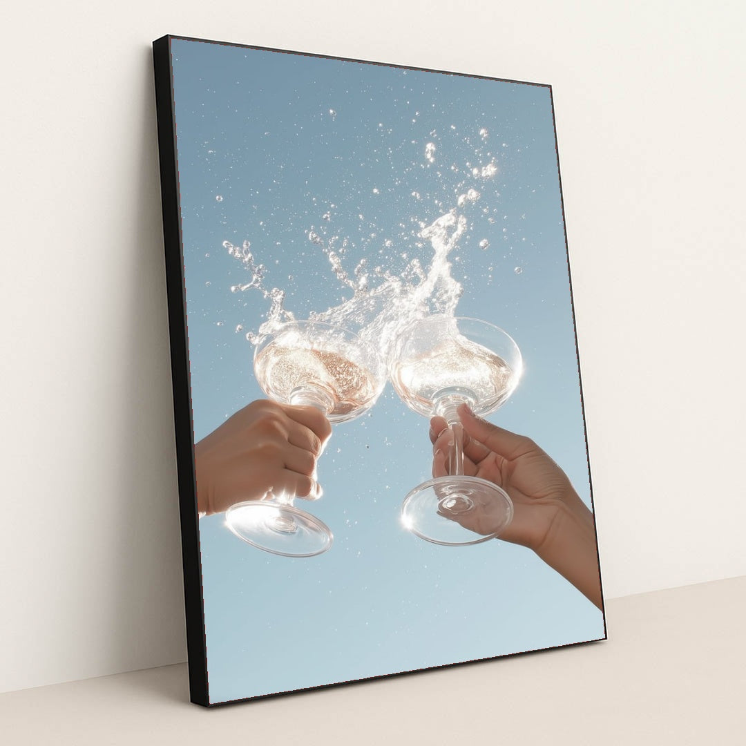 This artwork shows two hands clinking wine glasses with a splash against a clear blue sky, in a black frame.