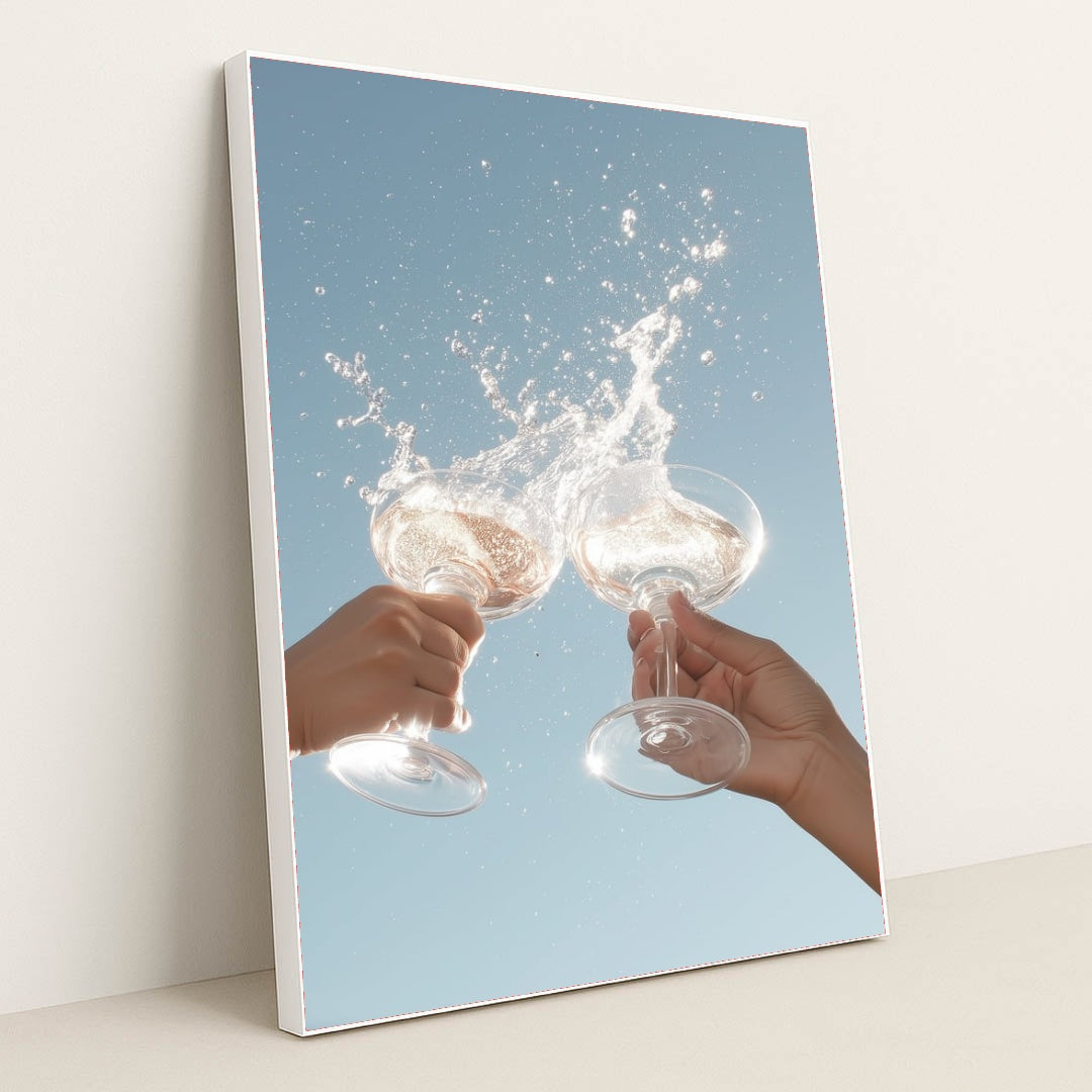 This artwork shows two hands clinking wine glasses with a splash against a clear blue sky, in a white frame.