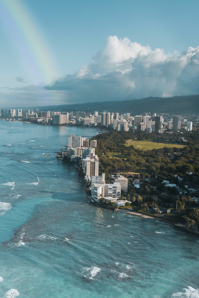 Jess Loiterton - A stunning aerial view of Honolulu's skyline with a rainbow over the ocean and cityscape.