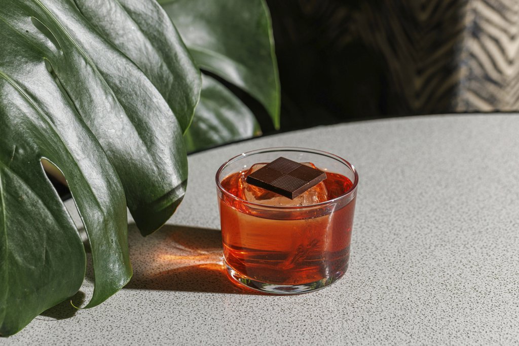 𝙊𝙎𝙑𝘼𝙇𝘿𝙊 𝙍𝙊𝙈𝙄𝙏𝙊 - A vibrant Negroni cocktail garnished with dark chocolate, perfect for an exotic beverage experience.