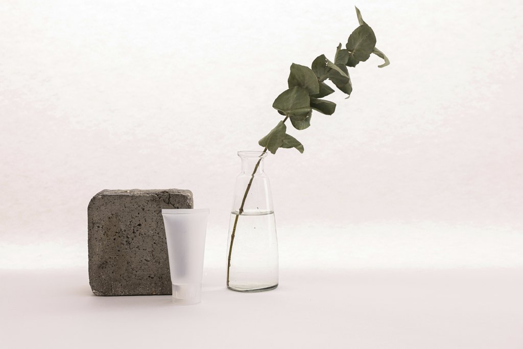 Cup of  Couple - A minimalist composition of skincare tube with a plant and concrete block on a white backdrop.