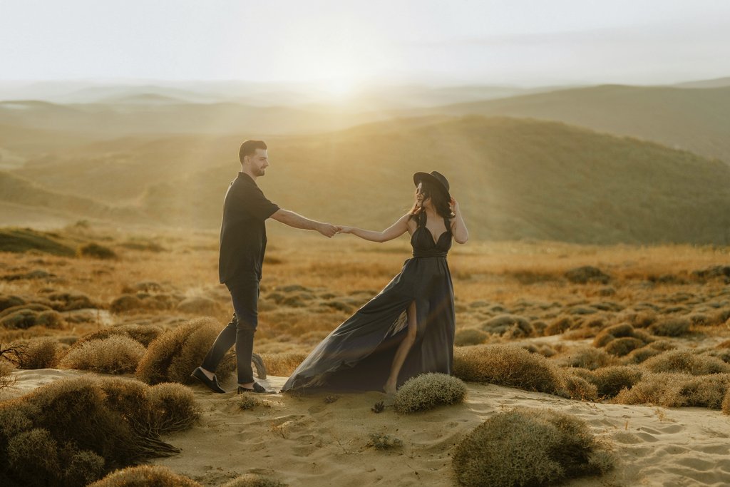 OĞUZHAN YAVUZ - A young couple holding hands in a desert landscape as the sun sets, creating a warm and elegant atmosphere.