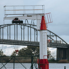 Nesshi Oliveira - View of an industrial crane with a backdrop of a Lisbon bridge over the river.