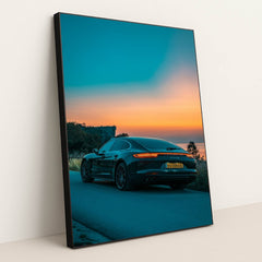 This photo shows the rear side of a dark Porsche Panamera 4S sedan parked on a road overlooking a colorful sunset, in a black frame.