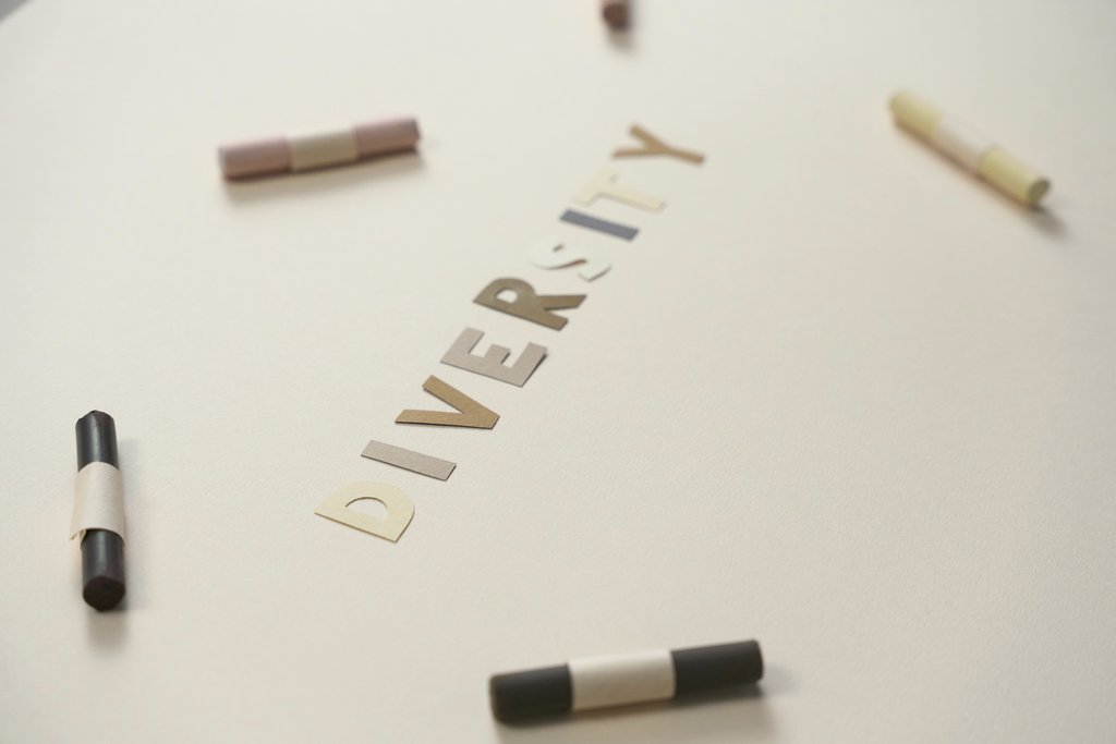 cottonbro studio - A close-up of colored crayons surrounding cut-out letters spelling 'diversity' on a white background.