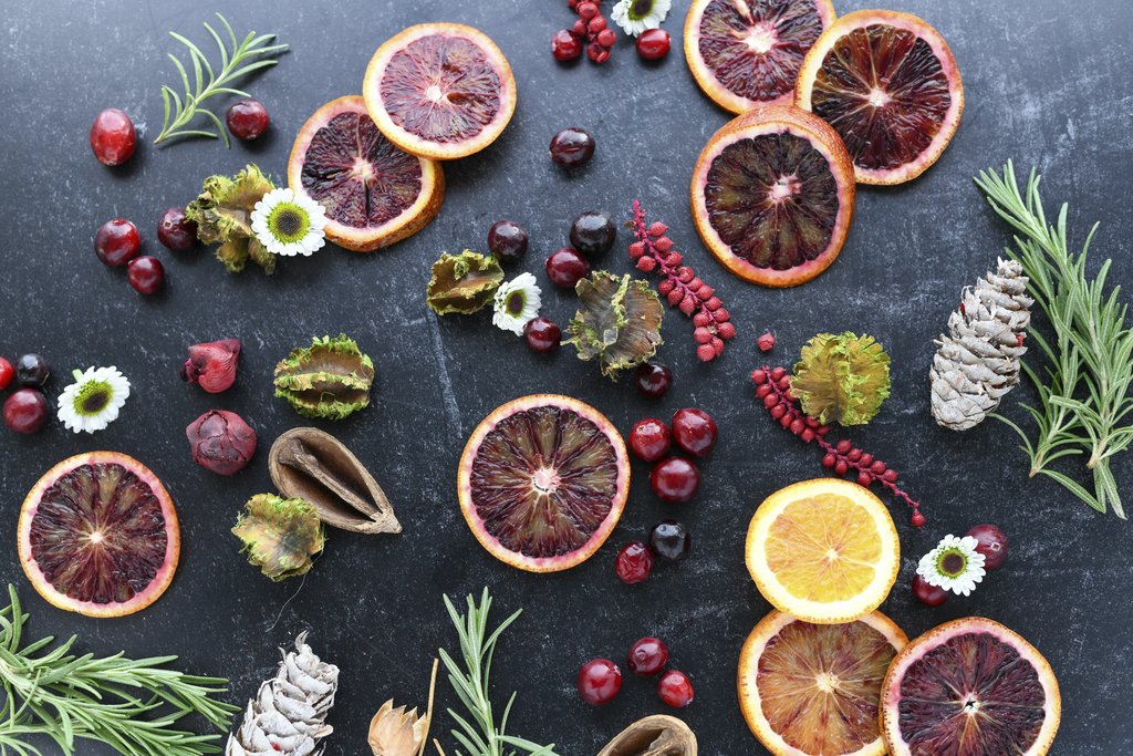 Heather Brock - A festive flat lay features blood oranges, pine cones, rosemary, and cranberries on a dark background.