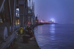 Ricardo Oliveira - Dusk at a bustling waterfront with a glowing Ferris wheel and shipyard ambiance.