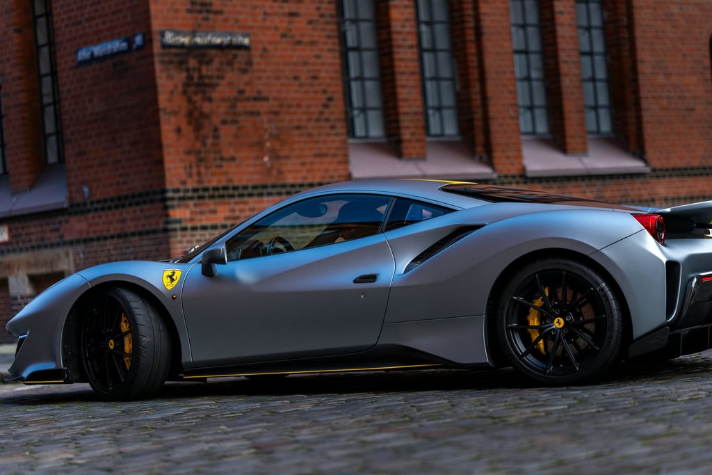 Ferrari 488 GTB in Silver Shine parked near a brick building, showcasing its sleek design and racing details.