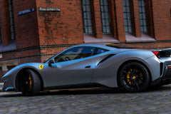 Ferrari 488 GTB in Silver Shine parked near a brick building, showcasing its sleek design and racing details.