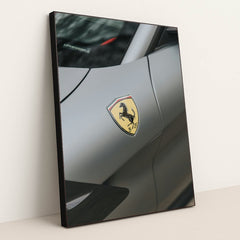This photo shows a close-up of the Ferrari prancing horse badge on the fender of a matte gray Ferrari, in a black frame.