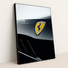 This photo shows a close-up of a Ferrari badge on a two-tone black and silver body panel, in a black frame.