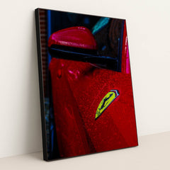 This photo shows the close-up of a red Ferrari’s fender and badge covered in rain droplets, in a black frame.