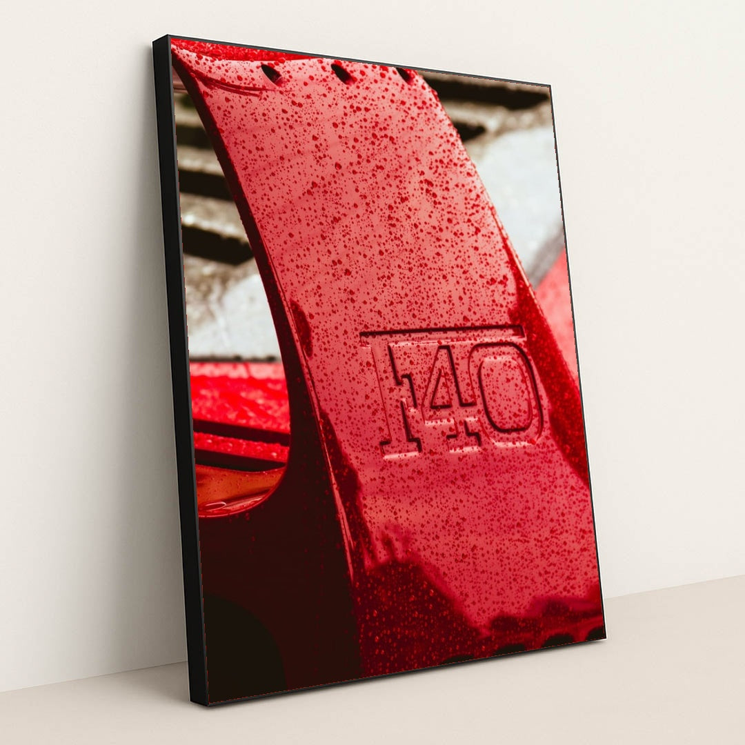 This photo shows a close-up of a wet red Ferrari F40 rear wing with raindrops, in a black frame.