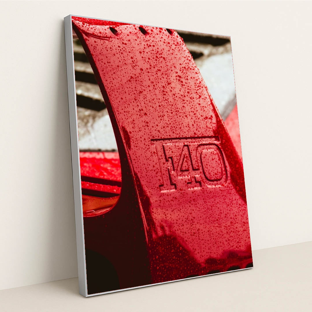 This photo shows a close-up of a wet red Ferrari F40 rear wing with raindrops, in a silver frame.