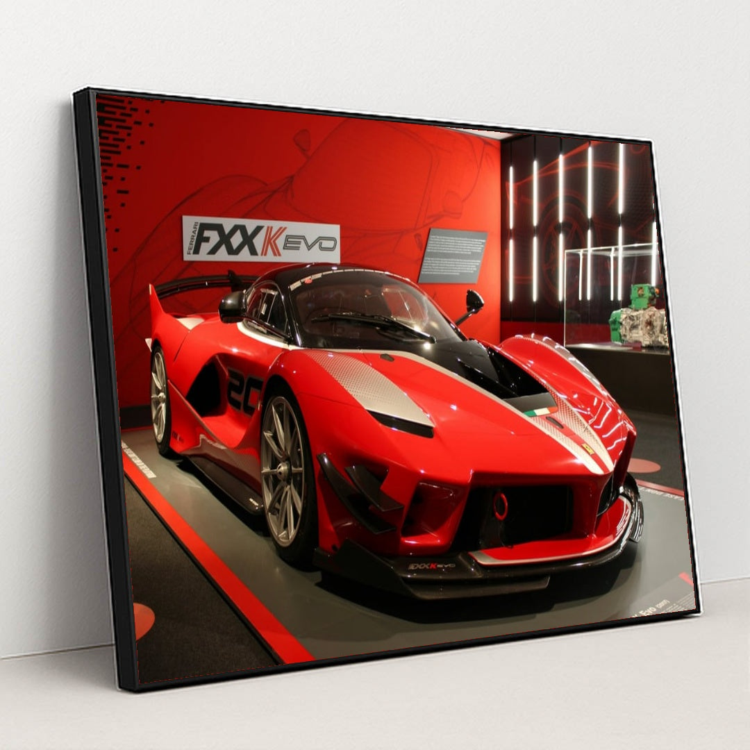 This photo shows a red Ferrari FXX-K Evo race car on display in a museum with red walls, in a black frame.