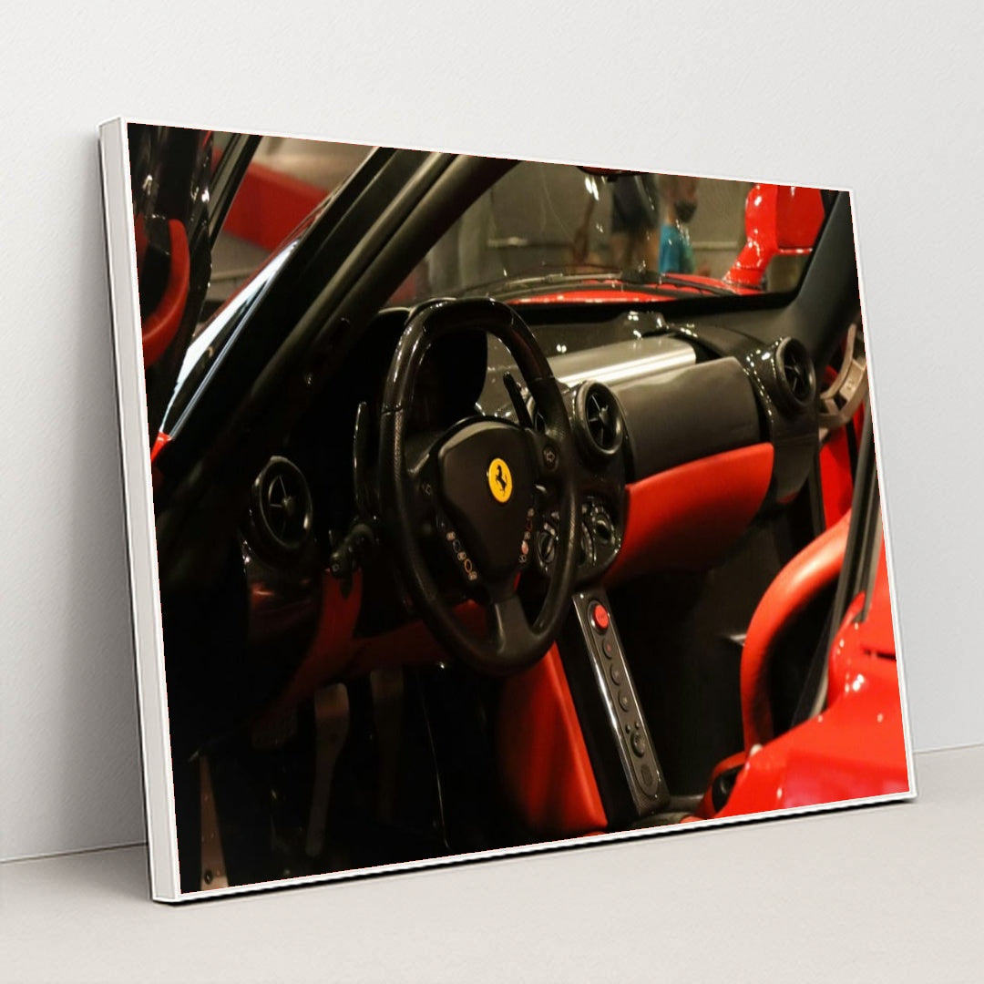 This photo shows the black and red leather interior of a Ferrari, featuring a round steering wheel and minimalist dash, in a white frame.