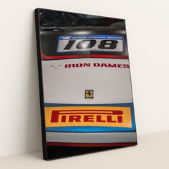 This photo shows a close-up of the hood of a Ferrari race car with Iron Dames and Pirelli logos, in a black frame.