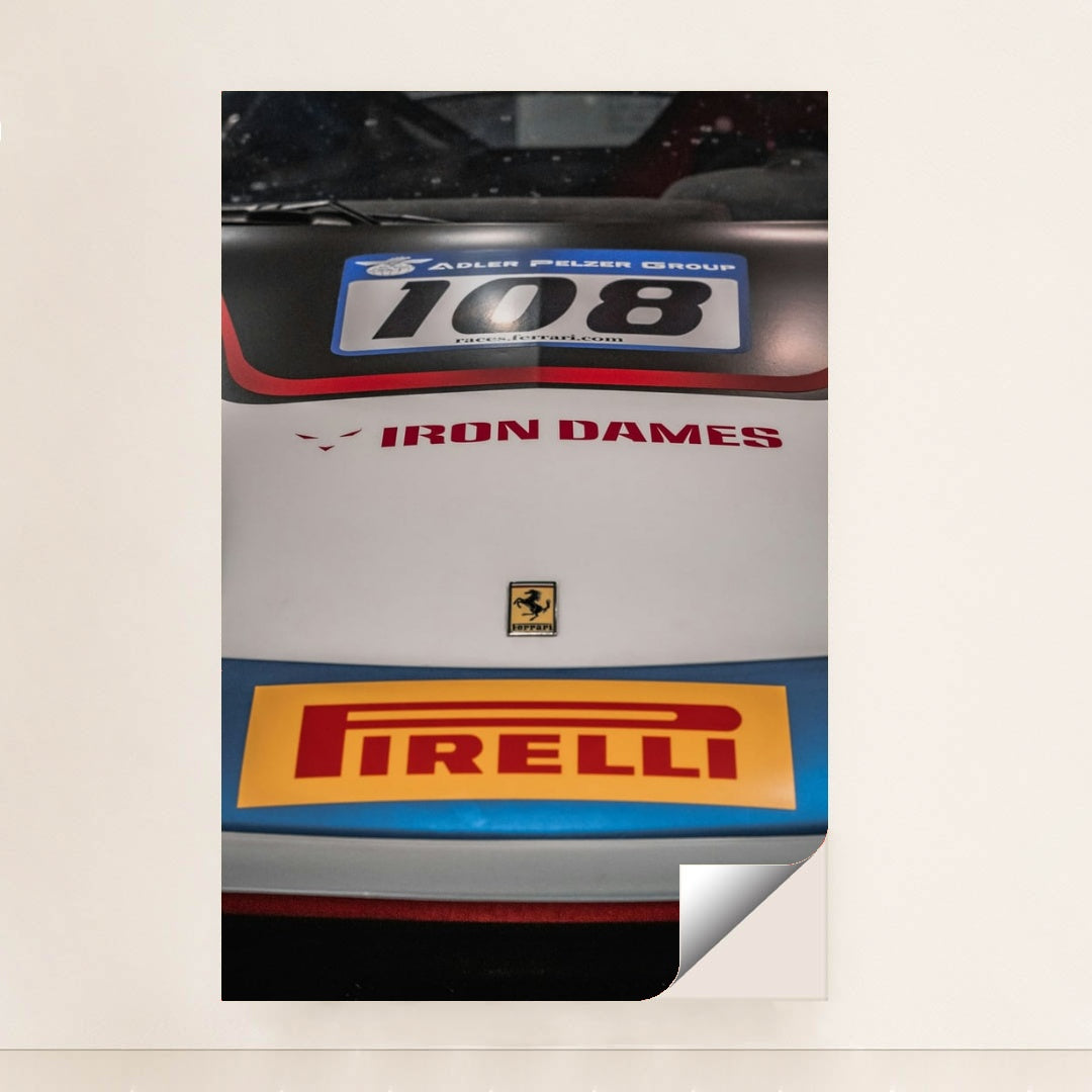 This photo shows a close-up of the hood of a Ferrari race car with Iron Dames and Pirelli logos, unframed style.