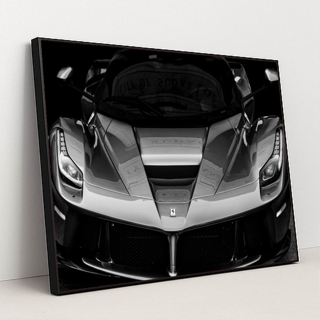 This photo shows the front view of a Ferrari hypercar in dramatic black and white, in a black frame.