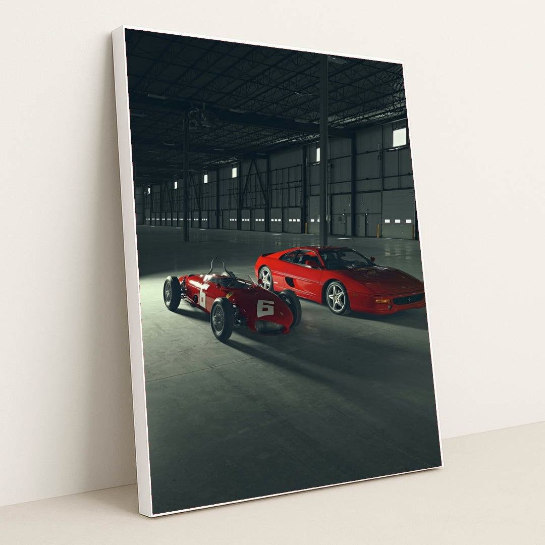This photo shows a vintage red Ferrari race car and a red Ferrari coupe parked inside a large industrial warehouse, in a white frame.