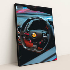 This photo shows the black carbon fiber steering wheel of a Ferrari, with red accents and dashboard controls, in a black frame.