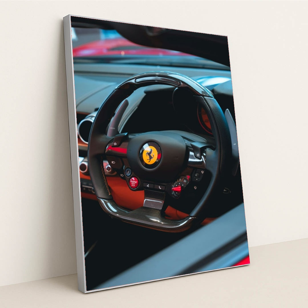 This photo shows the black carbon fiber steering wheel of a Ferrari, with red accents and dashboard controls, in a silver frame.